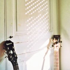 an acoustic guitar sitting in front of a white wall with sunlight coming through the window