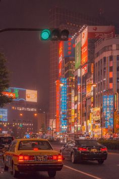 cars are stopped at an intersection in a city with tall buildings and neon signs on the walls