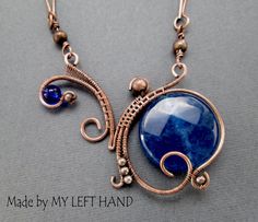 a wire wrapped necklace with a blue stone in the center and two small beads hanging from it