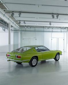 an old green car is parked in a large room with white walls and ceiling lights