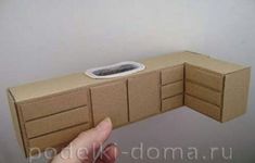 a hand is holding a cardboard box shaped like a kitchen sink and cupboards that are made out of cardboard