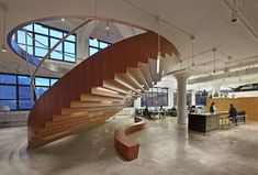 a spiral staircase in an office building with large windows and lots of desks around it