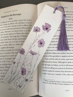 an open book with a tasseled bookmark and purple flowers on the page