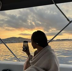 a woman is sitting on a boat and looking at her cell phone while the sun sets