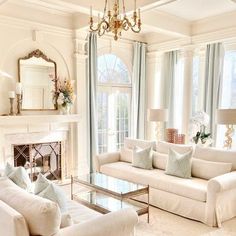 a living room filled with furniture and a fire place under a chandelier in front of a window