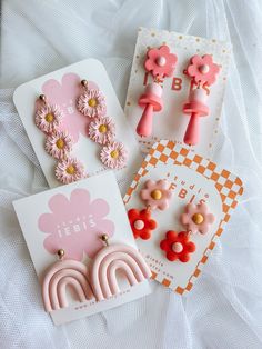 three pairs of pink and orange earrings on top of a white sheet