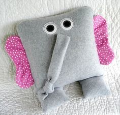 an elephant pillow with eyes and ears on top of a white bed sheet, next to a pink polka dot headband