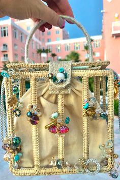 a hand holding a white purse with lots of beads and jewels on the handle, in front of a pink building