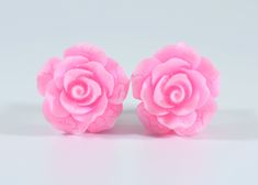 two pink roses sitting next to each other on top of a white surface with one flower in the middle