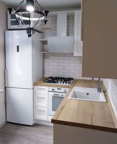 an empty kitchen with white appliances and wood counter tops, including a light fixture over the sink