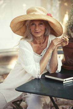 an older woman sitting at a table with a potted plant