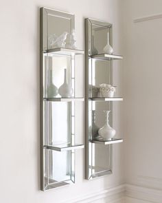 two mirrors mounted to the side of a wall next to vases and other items