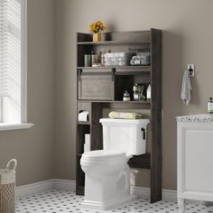 a white toilet sitting in a bathroom next to a wooden shelf filled with towels and other items