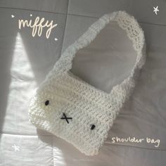 a white crocheted bag with a bunny face on the front and bottom, sitting on top of a sheet