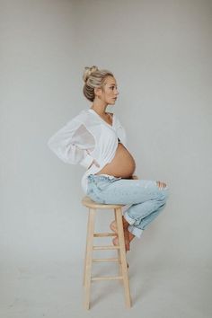 a pregnant woman sitting on top of a wooden stool with her hands behind her back