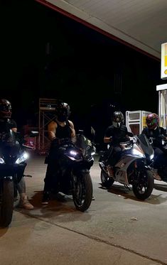 three people on motor bikes at night in front of a gas station with two men standing next to them