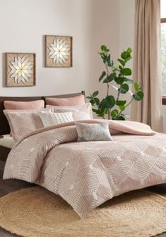 a bed with pink comforter and pillows in a bedroom next to a plant on the floor