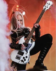 a woman with long hair and black boots is holding a white guitar in her hands