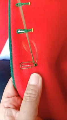 a person holding a piece of red material with green string attached to the top of it
