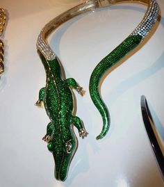 a green lizard brooch sitting on top of a white table next to a pair of scissors