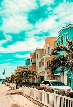 a row of colorful houses on the beach with cars parked along the sidewalk and palm trees lining the street