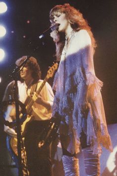 two people on stage with one holding a guitar and the other singing into a microphone