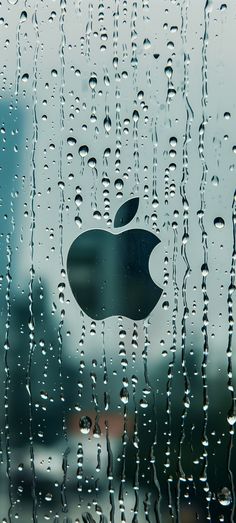an apple logo is seen through the raindrops on a glass window with buildings in the background