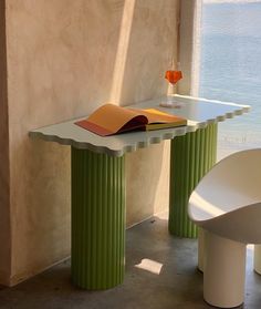 a table with a book on it next to some chairs and a window overlooking the water