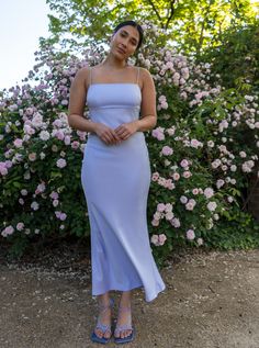 a woman standing in front of flowers wearing a blue dress with straps on the waist