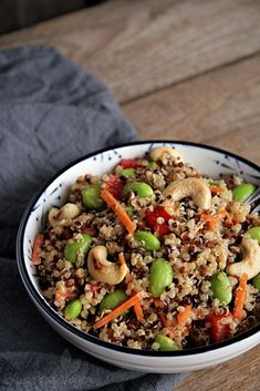 a bowl filled with rice and vegetables on top of a wooden table next to a gray napkin