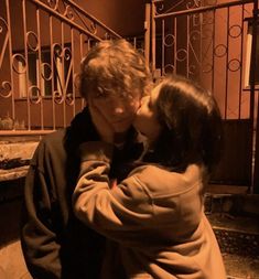 a man and woman standing next to each other in front of an iron gate with railings