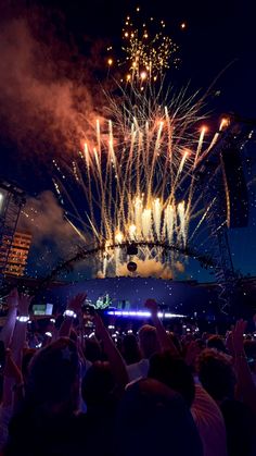 fireworks are lit up in the night sky above a crowd at an outdoor music festival