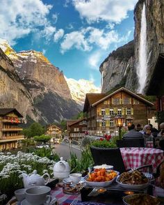 a table with food on it in front of a mountain range and waterfall, surrounded by mountains