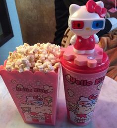 two hello kitty cups filled with popcorn on top of a table