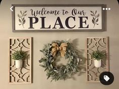 a welcome to our place sign hanging on the wall next to two small wreaths