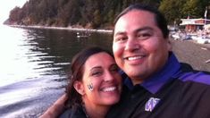 a man and woman smile at the camera while posing for a photo by the water