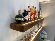 a shelf filled with lots of bottles and glasses on top of a wooden shelf next to a vase