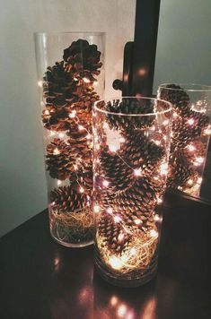 two glass vases filled with pine cones on top of a table