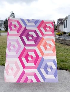 a very large quilt on the sidewalk in front of some grass and houses with trees