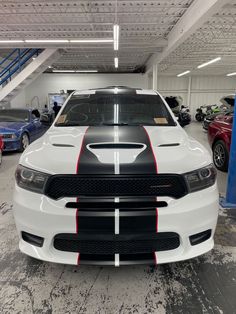 the front end of a white and black dodge charger in a garage with other cars