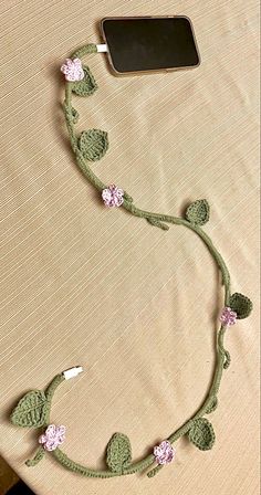 a cell phone is hooked up to a crocheted cord with flowers on it