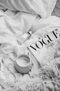 an open book sitting on top of a bed covered in white sheets and pillows next to a cup