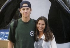 a young man and woman standing next to each other in front of a large bird sculpture