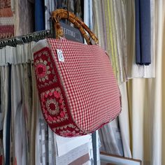 a red and white handbag hanging on a rack in front of some fabric samples