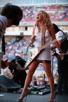 a woman with a guitar on stage in front of an audience at a music festival