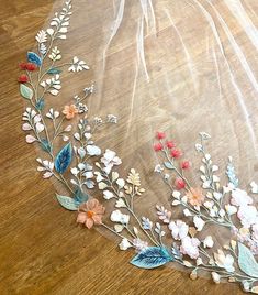 a veil with flowers and leaves on it sitting on top of a wooden floor in front of a window