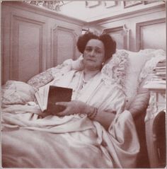 an old black and white photo of a woman sitting in a chair holding a book