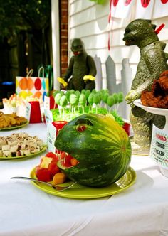 a table topped with watermelon and stuffed animals next to other foods on plates