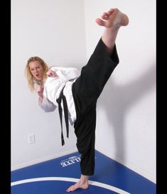 a woman in black pants and white shirt doing a trick on a blue mat with her feet up