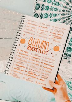 a hand holding an autumn bucket list in front of a wall with pumpkins on it